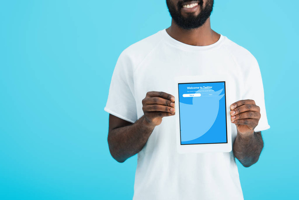 KYIV, UCRANIA - 17 DE MAYO DE 2019: vista recortada del hombre afroamericano mostrando tableta digital con aplicación de twitter, aislado en azul
 - Foto, Imagen