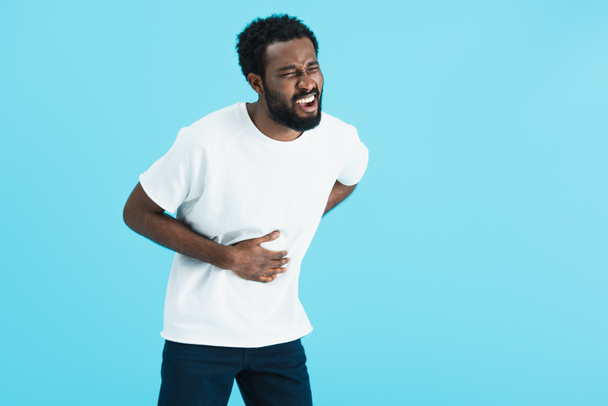 giovane uomo afroamericano in t-shirt bianca con dolore addominale, isolato su blu
   - Foto, immagini