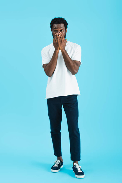 worried african american man in white t-shirt closing face, isolated on blue   - Fotó, kép