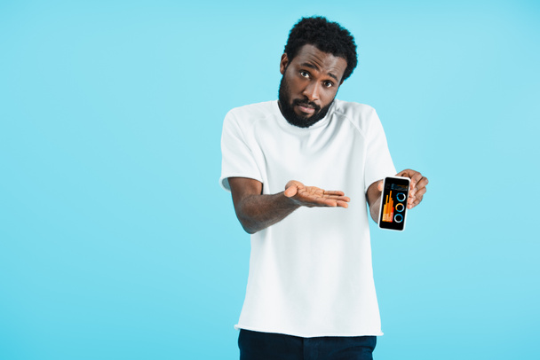 απογοητευμένος Αφρικανός Αμερικανός άνθρωπος δείχνει smartphone με app γραφικών, απομονώνεται σε μπλε - Φωτογραφία, εικόνα