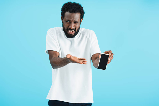 vystrašený afroamerický muž zobrazující smartphone s prázdnou obrazovkou, izolovaný na modrém - Fotografie, Obrázek