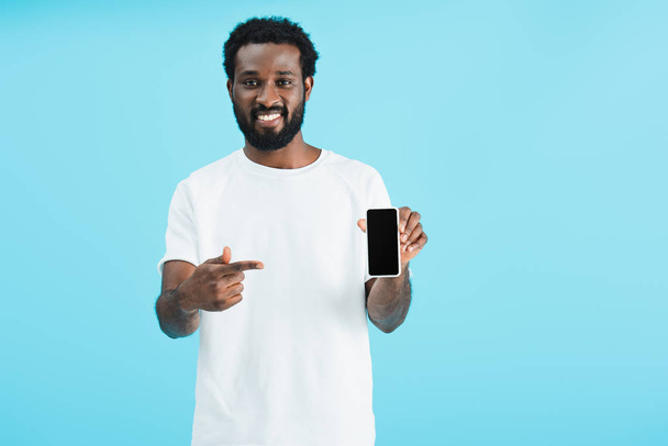 hombre americano africano alegre apuntando al teléfono inteligente con la pantalla en blanco, aislado en azul
 - Foto, imagen