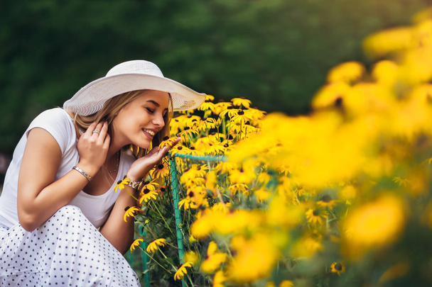 Hermosa mujer joven oliendo flor amarilla en el parque
. - Foto, imagen