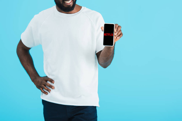 KYIV, UKRAINE - MAY 17, 2019: cropped view of african american man showing smartphone with netflix app, isolated on blue - Foto, Imagem