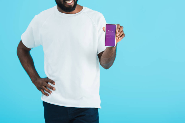 KYIV, UKRAINE - MAY 17, 2019: cropped view of african american man showing smartphone with instagram app, isolated on blue - Foto, afbeelding