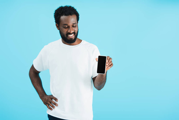 szczęśliwy African amerykański człowiek pokazując smartphone z pustym ekranem, izolowane na niebiesko - Zdjęcie, obraz