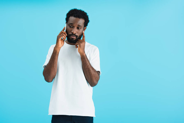 worried african american man talking on smartphone, isolated on blue - 写真・画像