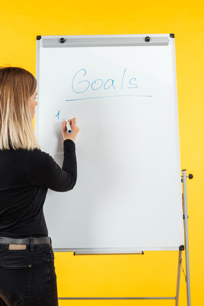 vue arrière de la femme d'affaires debout près de tableau à feuilles blanches, la liste des objectifs d'écriture
 - Photo, image
