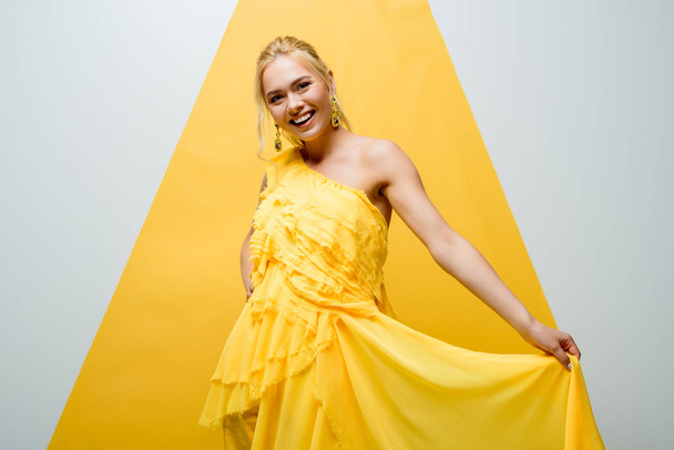 happy blonde girl smiling while posing and looking at camera on white and yellow  - Fotoğraf, Görsel