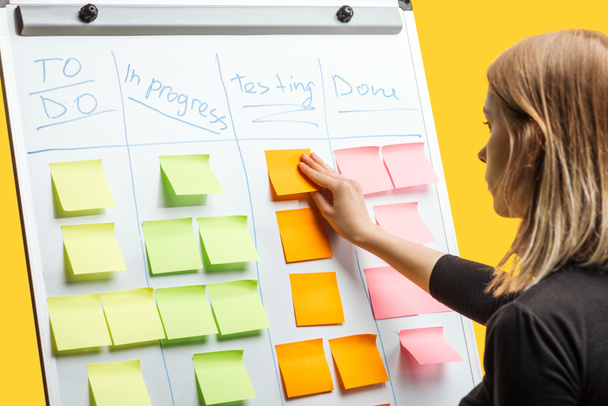 smart businesswoman standing near white flipchart, attaching sticky notes with copy space - Foto, Imagen