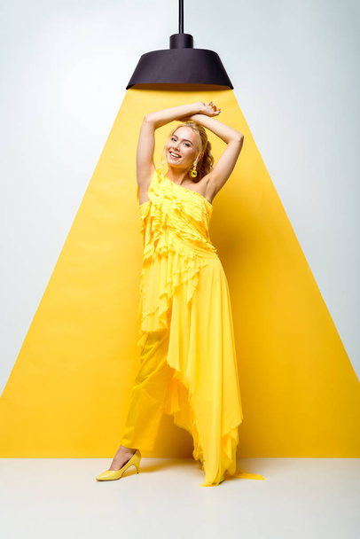happy young woman standing with hands above head and smiling on white and yellow  - Foto, Imagem