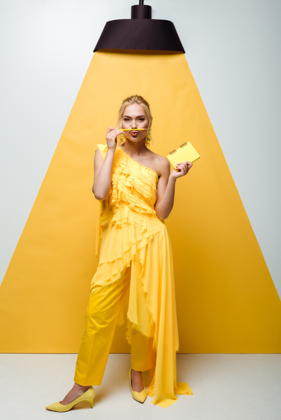 blonde woman with duck face holding pencil near mouth and notebook in hand on white and yellow  - Fotó, kép