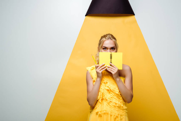 young blonde woman covering face with notebook on white and yellow - Photo, Image