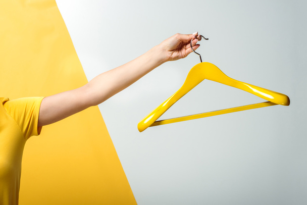 cropped view of woman holding wooden hanger on white and yellow  - Foto, afbeelding