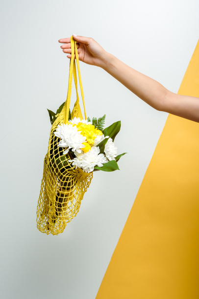 cropped view of  woman holding string bag with flowers on white and yellow  - Фото, изображение