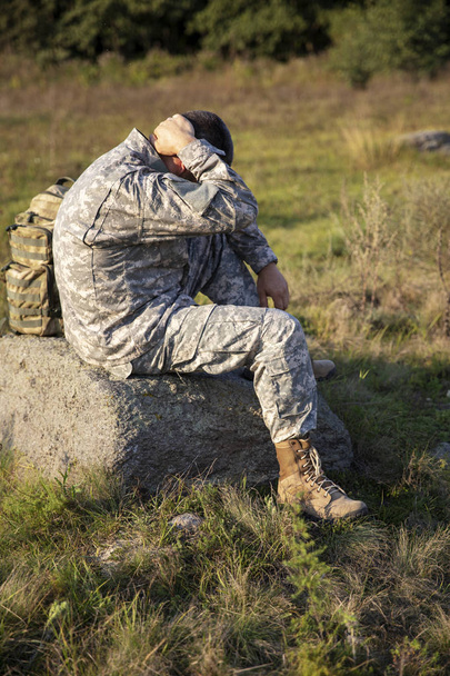 Ο στρατιώτης κάθεται και αναπαύεται. Λυπημένοι στρατιώτες. Κουρασμένος στρατιώτης. - Φωτογραφία, εικόνα