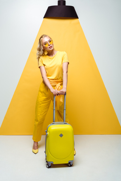 beautiful woman in sunglasses posing near luggage on white and yellow  - Fotografie, Obrázek