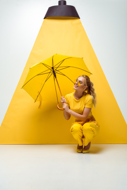 chica rubia feliz sosteniendo paraguas mientras está sentado en blanco y amarillo
  - Foto, Imagen