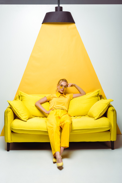 attraktive blonde Frau sitzt auf dem Sofa und blickt in die Kamera auf weiß-gelb  - Foto, Bild