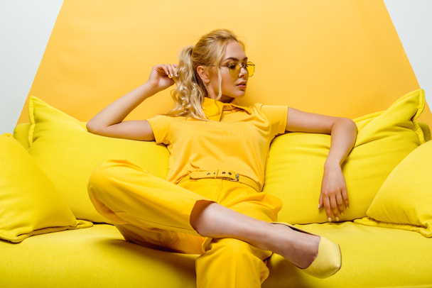 jolie femme blonde assise sur le canapé et touchant les cheveux sur blanc et jaune
  - Photo, image