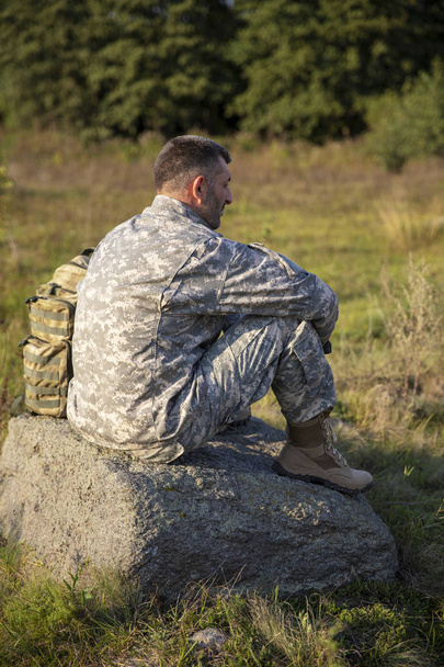 Ο στρατιώτης κάθεται και αναπαύεται. Λυπημένοι στρατιώτες. Κουρασμένος στρατιώτης. - Φωτογραφία, εικόνα