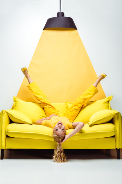 happy blonde woman lying upside down on sofa on white and yellow  - 写真・画像