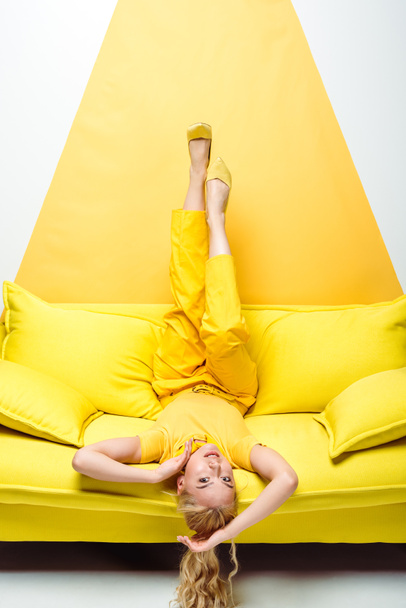 приваблива блондинка лежить догори ногами на дивані на білому і жовтому
  - Фото, зображення
