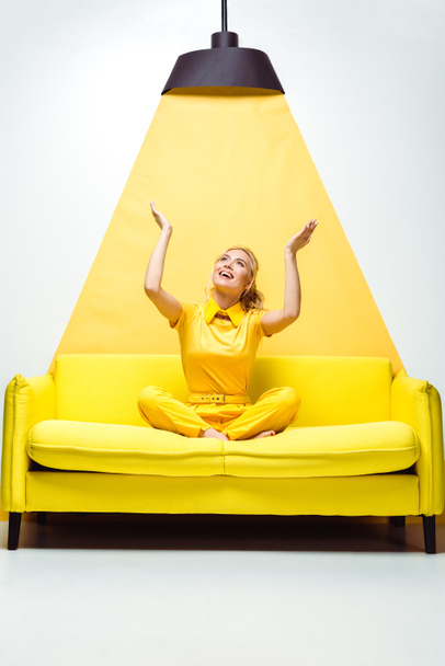 boldog szőke lány ül a kanapén kézzel feje fölött a fehér és sárga  - Fotó, kép