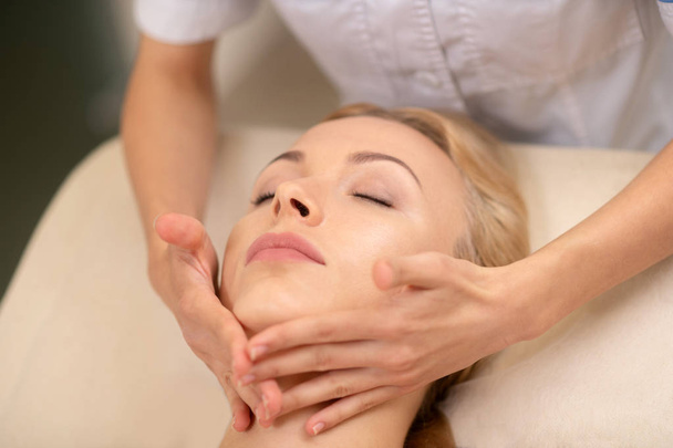 Blonde woman enjoying face massage in beauty salon - Fotografie, Obrázek