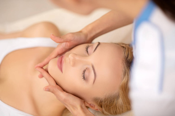 Woman closing her eyes while enjoying face massage - Φωτογραφία, εικόνα