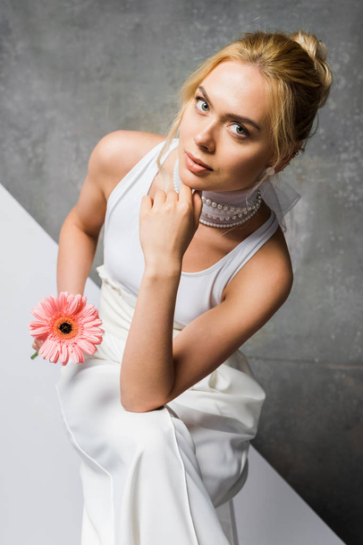 overhead view of pretty girl sitting and holding pink flower on white and grey  - Foto, afbeelding