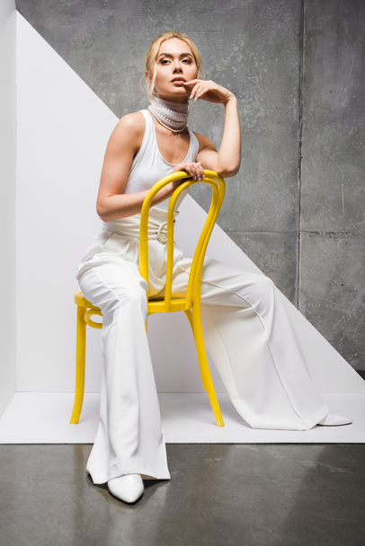 stylish and attractive blonde woman sitting on yellow chair on white and grey  - Foto, immagini