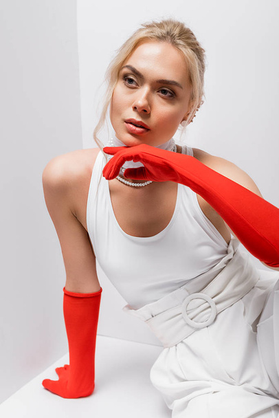 pretty and stylish woman in red gloves sitting on white  - Фото, зображення