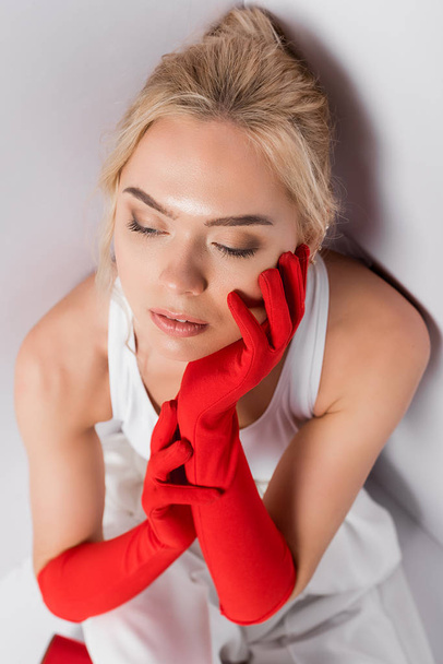 attractive blonde woman in red gloves touching face on white  - Fotoğraf, Görsel