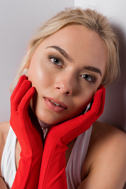 pretty blonde woman in red gloves touching face on white  - Photo, Image