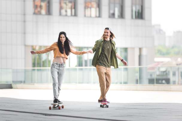 happy man holding hands with woman, riding on skateboard in city - Photo, image