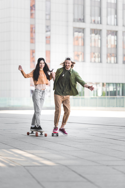 happy man holding hands with beautiful woman, riding on skateboard in city - Foto, afbeelding