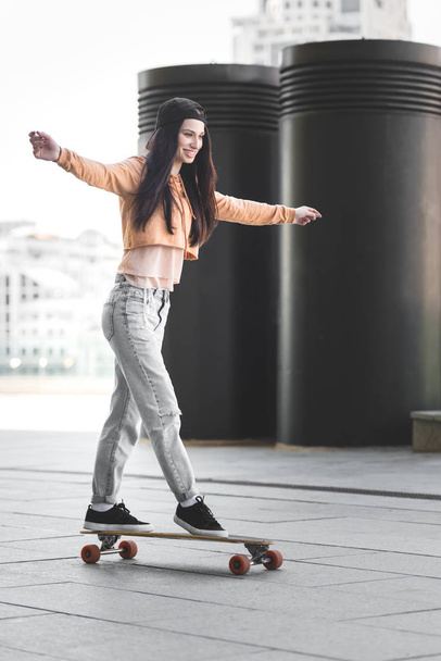 happy woman with outstretched hands riding on skateboard in city - Photo, Image