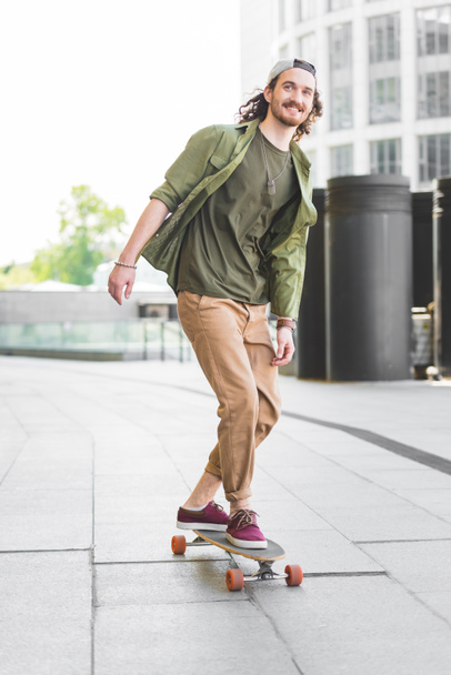 happy man in casual wear riding on skateboard in city, looking away - Zdjęcie, obraz