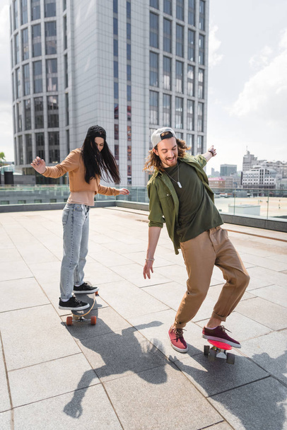 happy man with beautiful woman riding on skateboards on roof - Фото, изображение