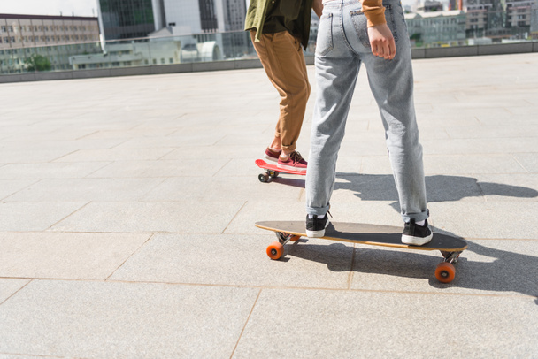 cropped view of man and woman riding on skateboards - 写真・画像