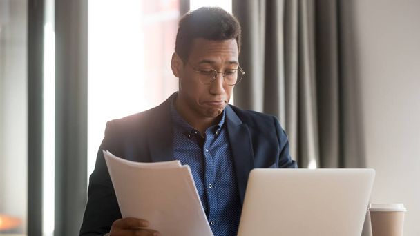 Confused black male employee feel unsure reading paperwork documents - Valokuva, kuva