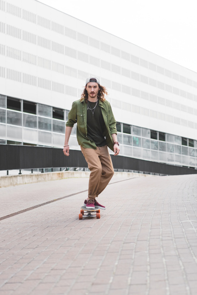 handsome man in casual wear riding on skateboard at street - Photo, Image