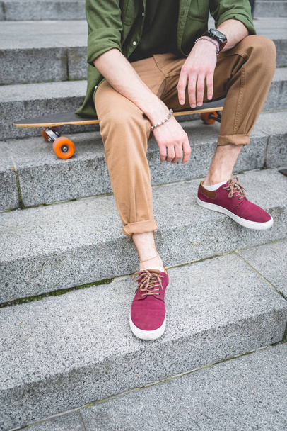 cropped view of man sitting on skateboard at stairs - Foto, imagen