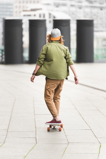 back view of man riding on skateboard at rooftop - Zdjęcie, obraz