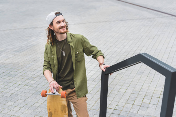 high angle view of happy man in casual wear with skateboard standing on street, looking away - Fotoğraf, Görsel