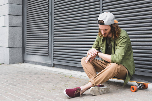 bel homme assis sur skateboard, regardant smartwatch
 - Photo, image