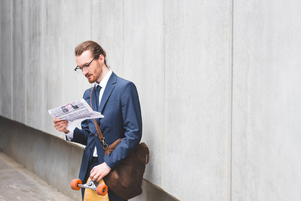 calm businessman in formal wear standing near skateboard, reading newspaper - Foto, Bild