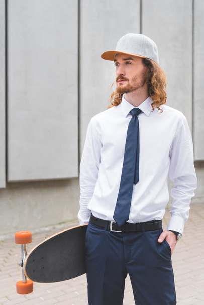calm businessman standing with skateboard at street, looking away - Foto, Bild
