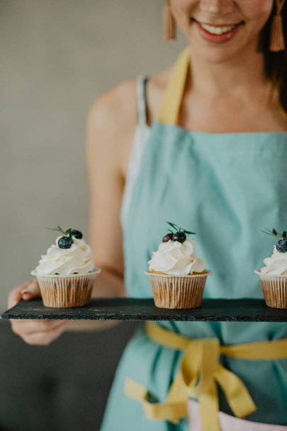 Beautiful woman in apron holding board with cupcakes - Φωτογραφία, εικόνα
